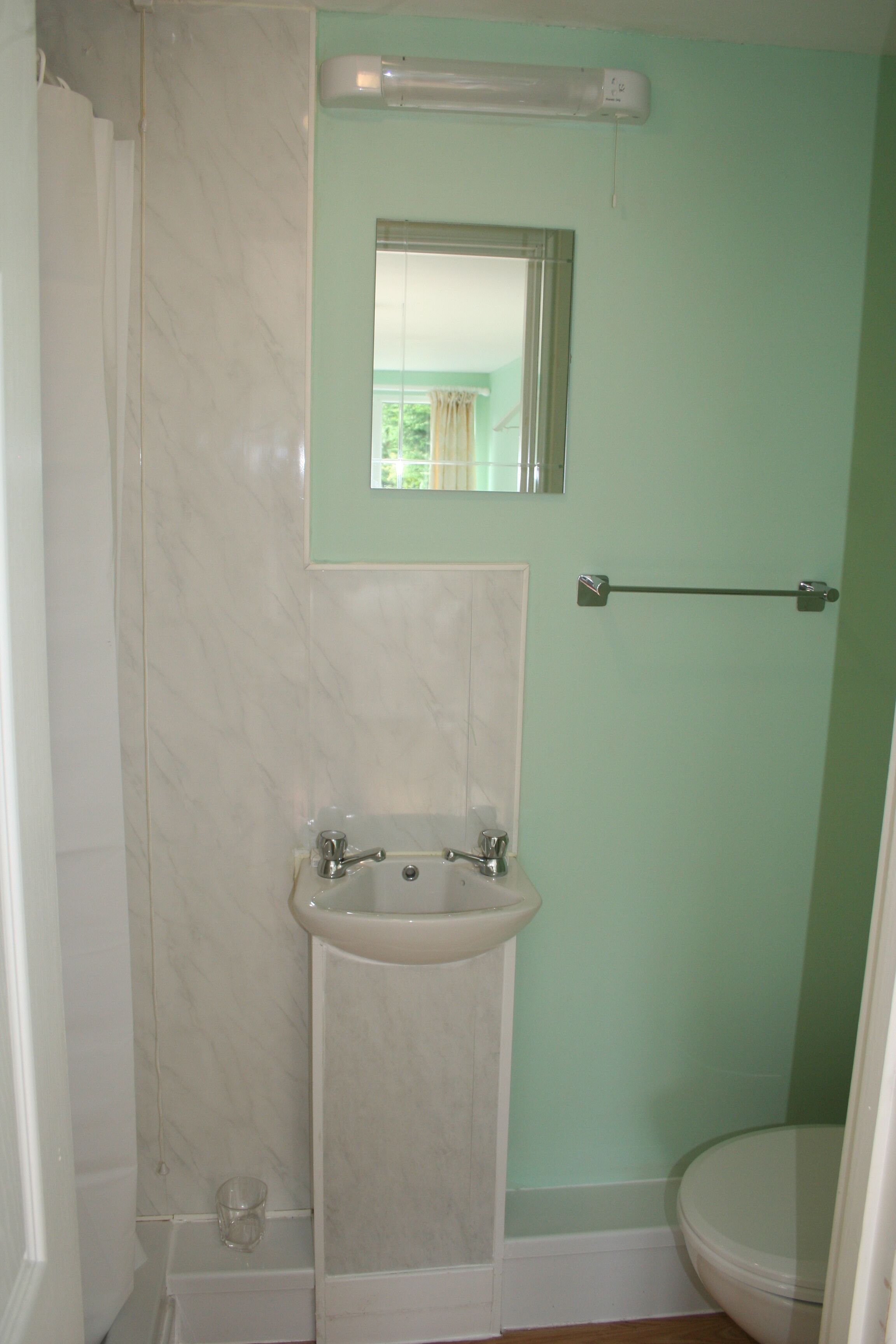 Un baño con lavamanos, espejo, toallero y retrete.