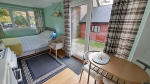 A bedroom with a bed, a chair, a table, and a view of the outside. - The Pines Cabin (Swansea)