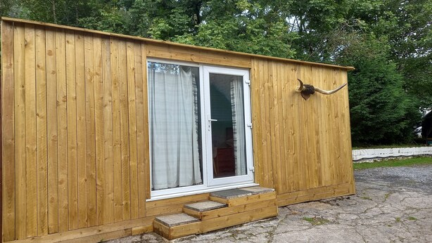 A wooden cabin with a sliding glass door, a small porch, and a wooden doorbell. - The Pines Cabin (Swansea)