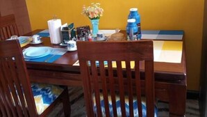 A dining area with a yellow wall, wooden chairs, a table set with plates, a vase of flowers, and a water dispenser. - Cosy homes ltd (Mlolongo)