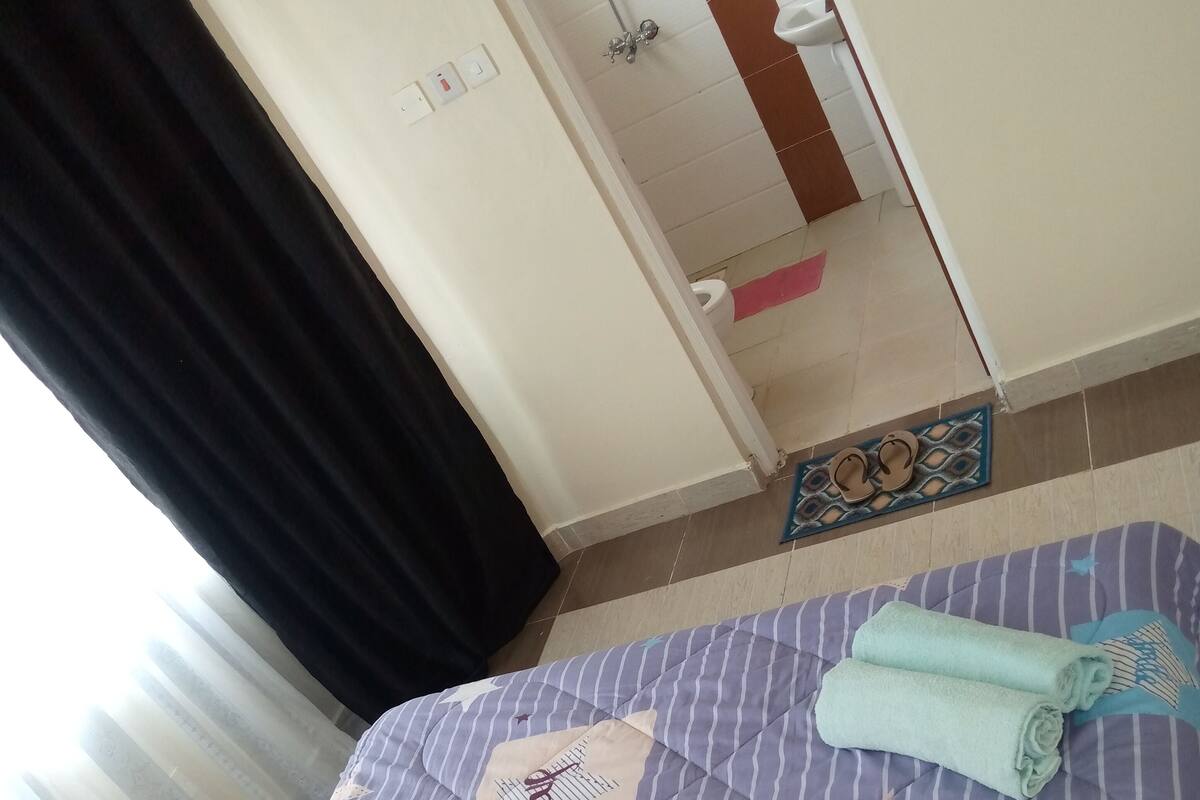 Una habitación de hotel con cama, baño visible a través de una puerta abierta y suelo de baldosas.