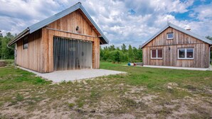 Two wooden buildings with large garage doors, surrounded by a grassy field and trees. - Zagroda nad Krutynią by Interhome (Spychowo-Kierwik)