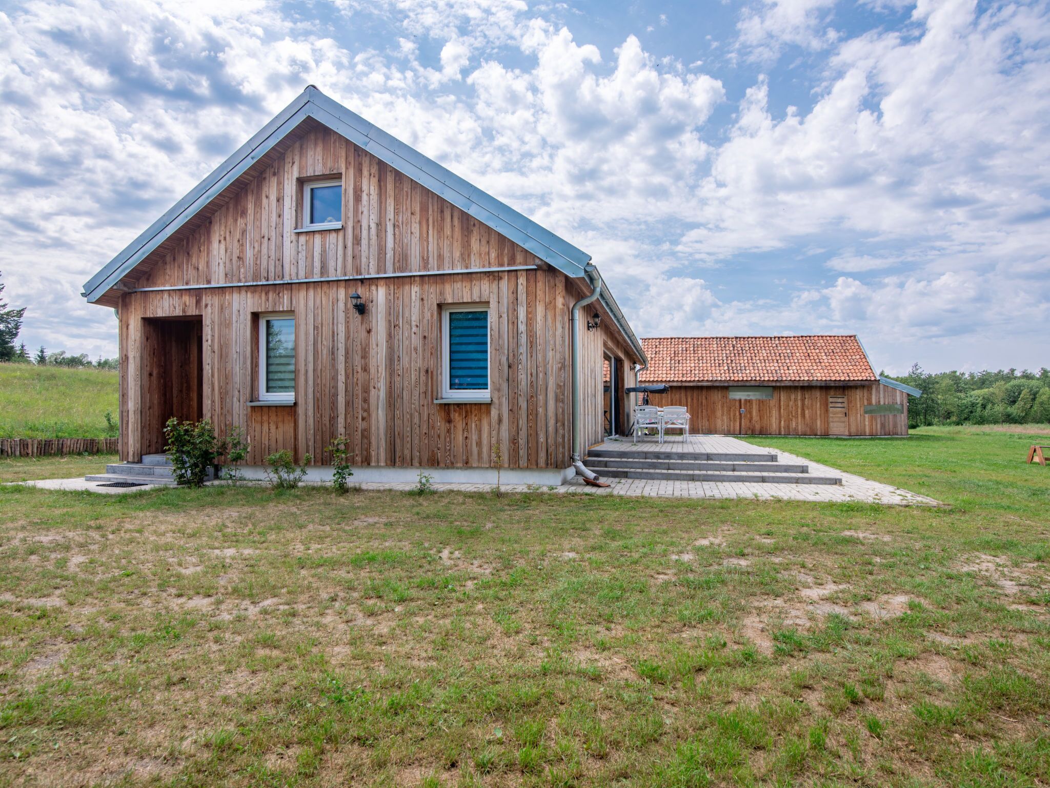 A wooden barn with a sloped roof and a smaller adjacent building with a red-tiled roof.