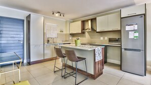 A modern kitchen with a central island, bar stools, a refrigerator, and a microwave. - 2 Bedroom Apartment in Century City (Cape Town)