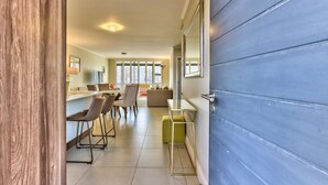 A modern kitchen with a blue accent wall, a dining area with chairs and a table, and a large window with blinds. - 2 Bedroom Apartment in Century City (Cape Town)