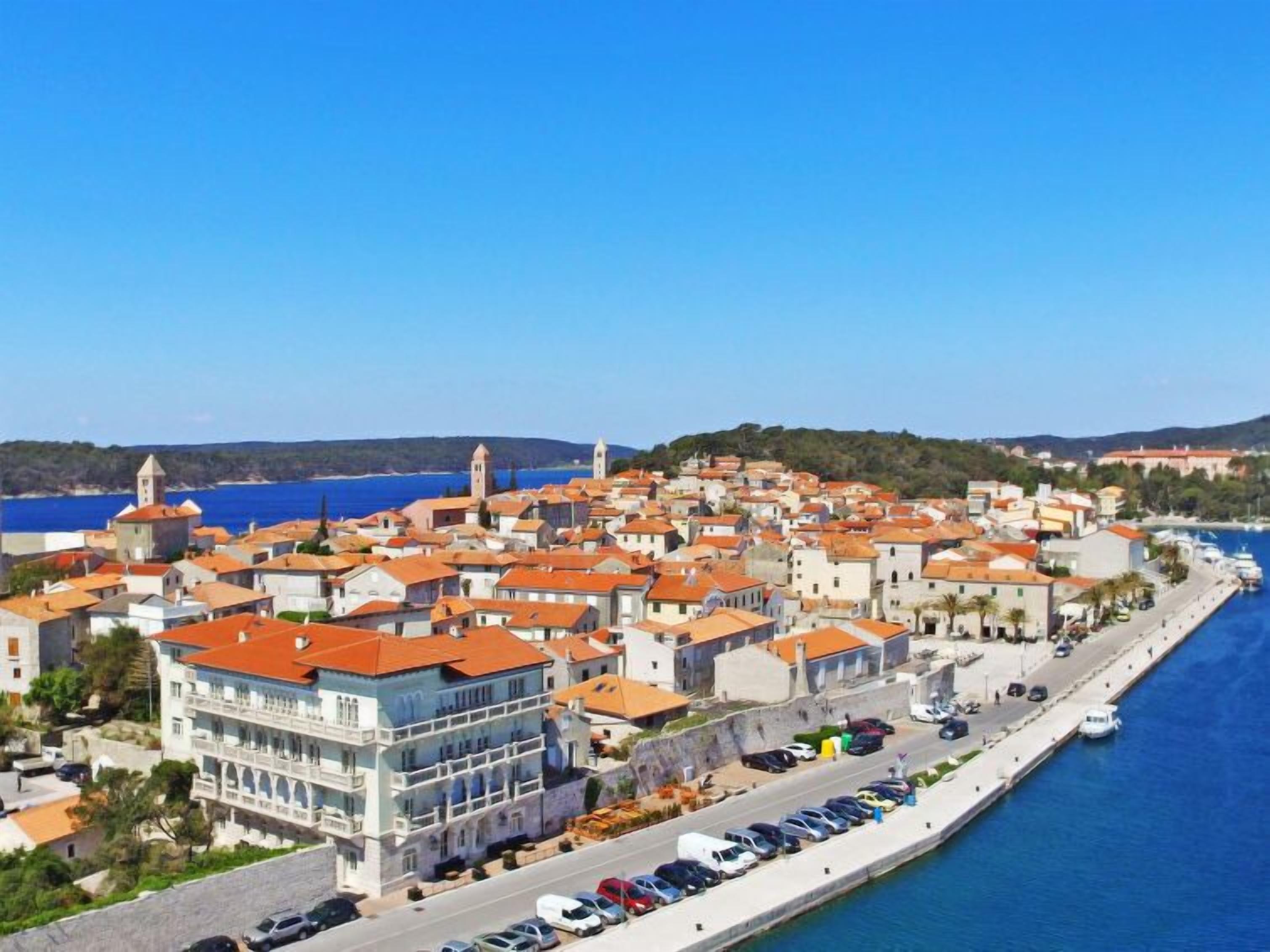 Un pueblo costero con edificios históricos, un puerto deportivo y un mar azul cristalino.