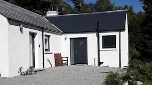 A modern white building with a gravel driveway, a wooden chair, and a door. - Lovely House Near Loch Ness in Scotland, UK (Inverness)