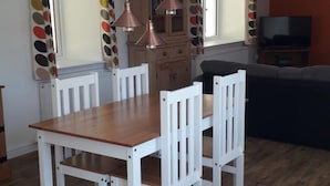 A dining area with a wooden table and white chairs, a kitchen with wooden cabinets, and a dark-colored sofa. - Lovely House Near Loch Ness in Scotland, UK (Inverness)