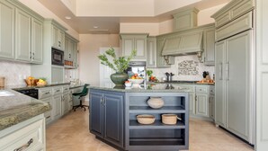 A kitchen with light green cabinets, a central island with a sink, and a microwave above it.