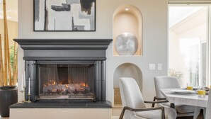 A modern living room with a fireplace, a dining area, and a large abstract painting on the wall.
