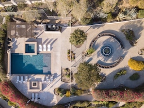 Eine Luftaufnahme eines Resorts mit Schwimmbad, Liegestühlen, einem kreisförmigen Garten und angelegten Grünflächen.