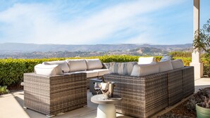 A covered outdoor seating area with wicker furniture and a table, overlooking a scenic landscape.