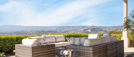 Un espacio de estar al aire libre cubierto con muebles de mimbre y una mesa, con vistas a un paisaje pintoresco.