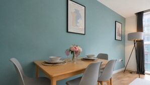 A dining area with a wooden table, grey chairs, a vase with flowers, and framed artwork on the wall.