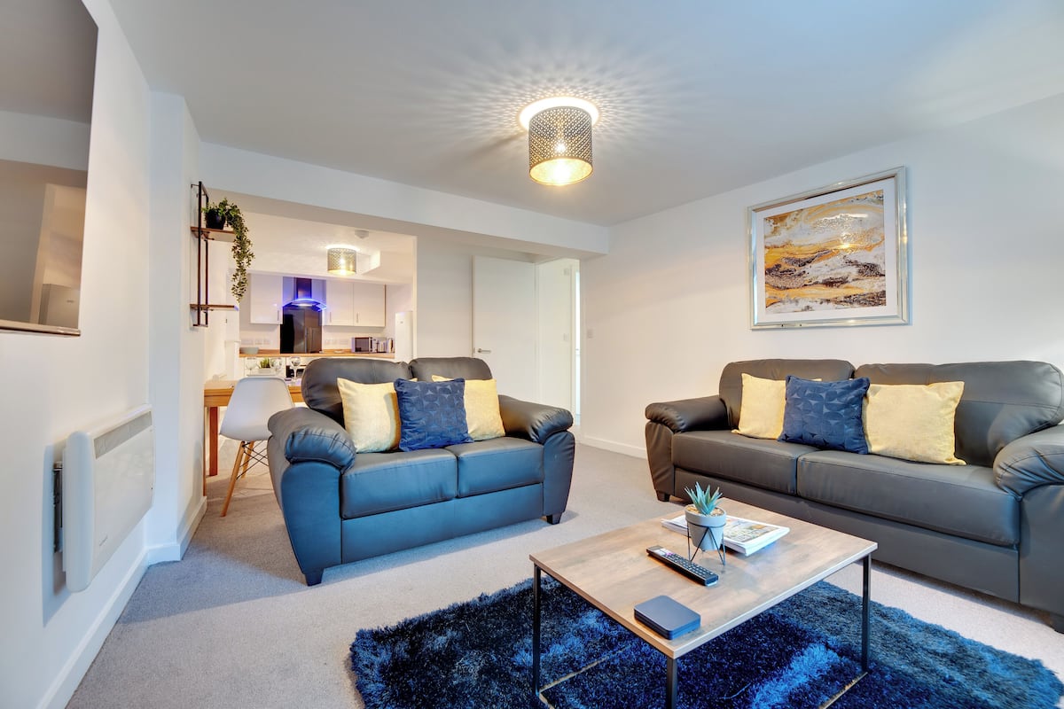 A modern living room with two sofas, a coffee table, and a kitchen in the background.