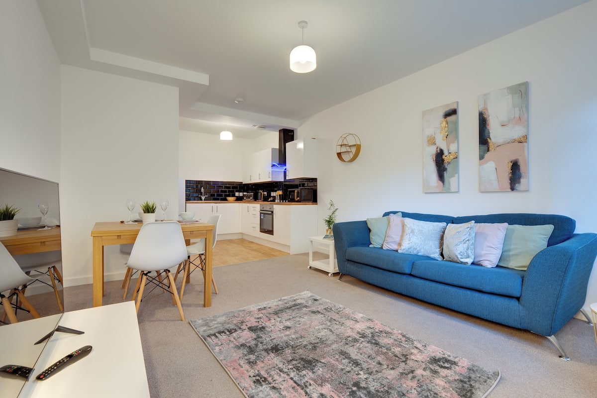 A modern living room with a blue sofa, a dining table, and a kitchen in the background.