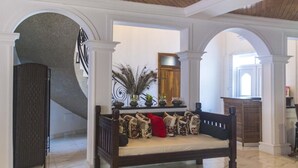 A lobby with a marble floor, a wooden bench with patterned cushions, and a staircase with a metal railing. - The Haven Boutique Hotel - Kumasi, Ghana (Ejisu)