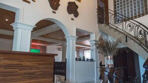 A spacious lobby with a wooden reception desk, a staircase with ornate railings, and a large potted plant. - The Haven Boutique Hotel - Kumasi, Ghana (Ejisu)