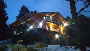 A log cabin with a stone exterior, multiple windows, and a snow-covered ground.