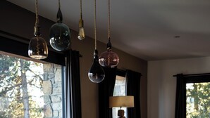 A dining area with a wooden table, black chairs, hanging pendant lights, and a view through a large window. - Vaste et Prestigieux Chalet à Font Romeu Pyrénées 2000 (Bolquère)