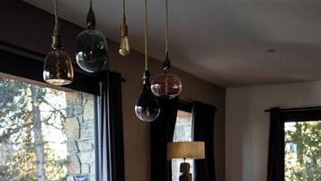 A dining area with a wooden table, black chairs, hanging pendant lights, and a view through a large window.