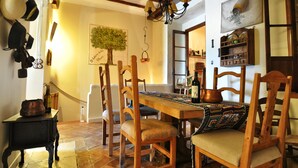 A dining area with a wooden table, chairs, and a chandelier. There is a wall-mounted shelf with bottles and a framed picture. - THE BALCONY OF THE OLIVE TREES (Luque)