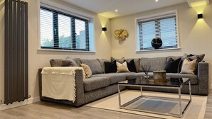 A modern living room with a sectional sofa, a glass coffee table, and two wall-mounted light fixtures. - Impeccable Farm Apartment in Walberton, England (Arundel)