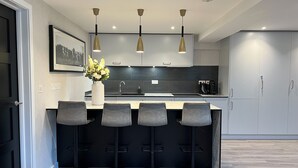 A modern kitchen with a central island, bar stools, pendant lighting, and a framed picture on the wall. - Impeccable Farm Apartment in Walberton, England (Arundel)