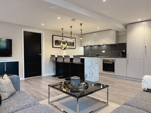 A modern living room with a glass coffee table, grey sofas, and a TV mounted on the wall. - Impeccable Farm Apartment in Walberton, England (Arundel)