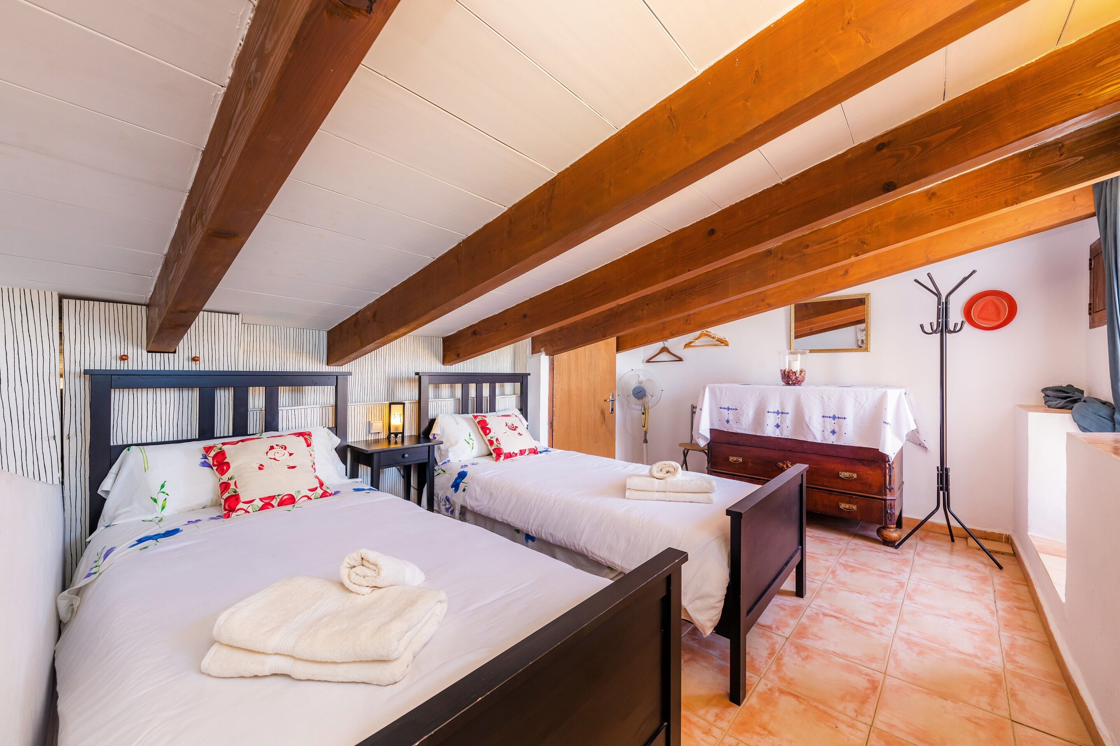 Een slaapkamer met twee bedden, houten balken, een nachtkastje, een dressoir en een spiegel.