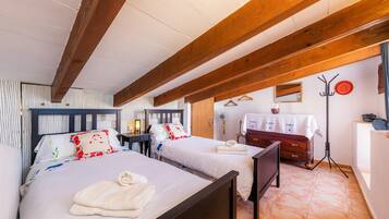 Een slaapkamer met twee bedden, houten balken, een nachtkastje, een dressoir en een spiegel.