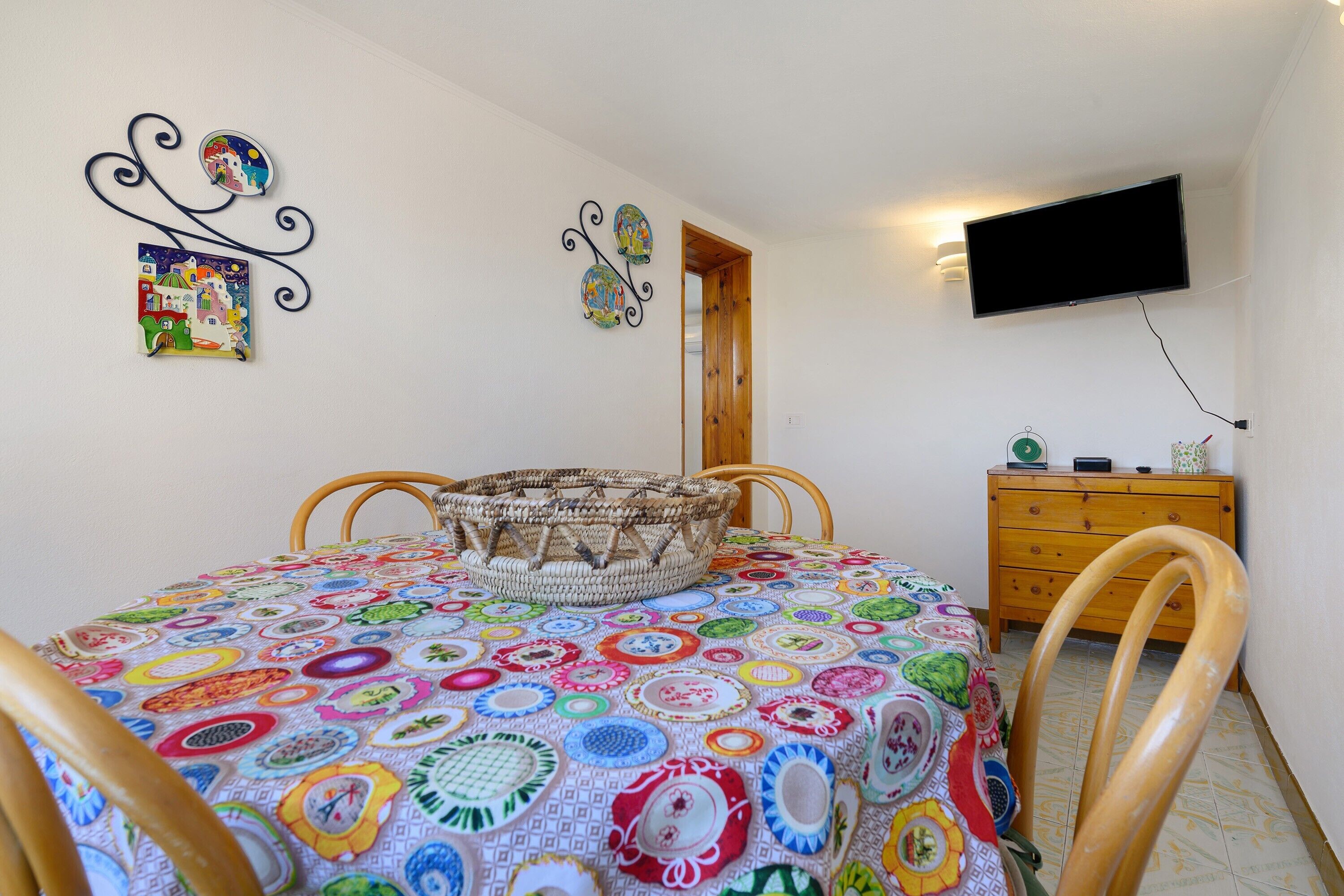 Ein Zimmer mit einem Bett, einem an der Wand befestigten Fernseher, einer Holzkommode und einer Tür zu einem anderen Raum.