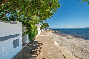 A coastal walkway with a white building, trees, and a clear view of the sea.