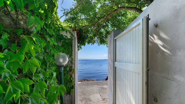 Un chemin menant à une porte de garage blanche, d’où l’on aperçoit la mer.