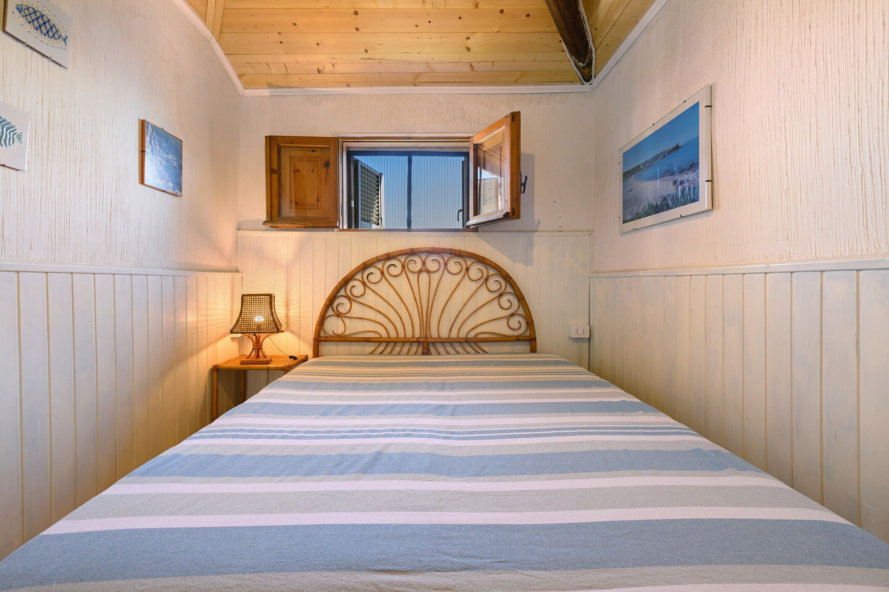 Une chambre à coucher avec un lit, une fenêtre, une lampe et un tableau au mur.