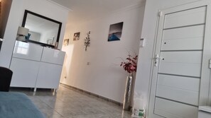 Una habitación con una cama, un armario blanco, un espejo, un jarrón con flores y una puerta.