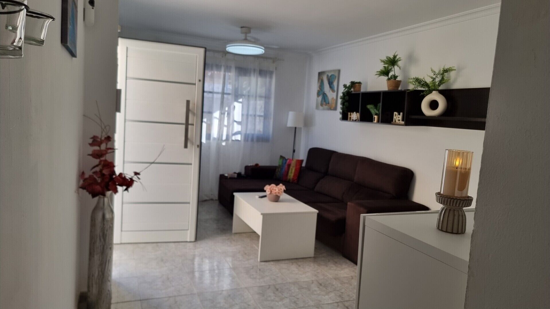 A living room with a sofa, a coffee table, a white cabinet, a door, a ceiling fan, and a wall with shelves.
