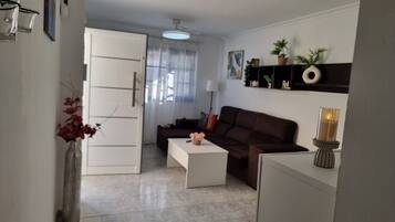 A living room with a sofa, a coffee table, a white cabinet, a door, a ceiling fan, and a wall with shelves.