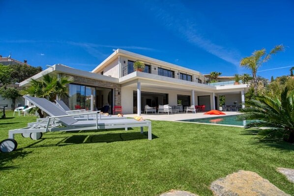 Une maison moderne à deux étages, dotée d’un grand patio, d’une piscine et d’une pelouse bien entretenue.