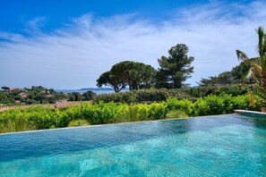 Une piscine d’eau cristalline, d’un bleu éclatant, avec vue sur la mer et les collines lointaines.
