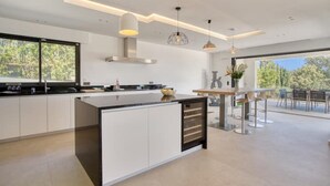 Een moderne keuken met een centraal eiland, grote ramen en een eetgedeelte met buitenplaatsing.