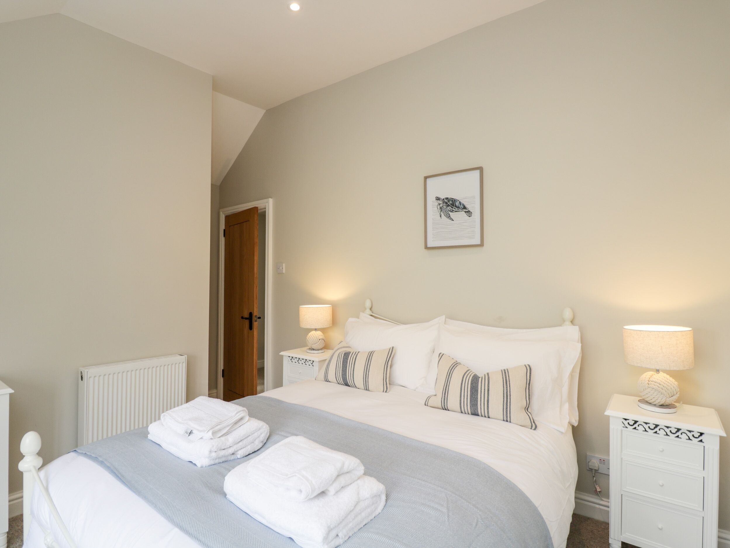A bedroom with a bed, two bedside tables, a radiator, a door, and a framed picture on the wall.