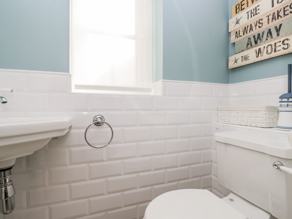 A bathroom with white tiles, a sink, a toilet, and a window. - Fisherbridge Cottage (Weymouth)