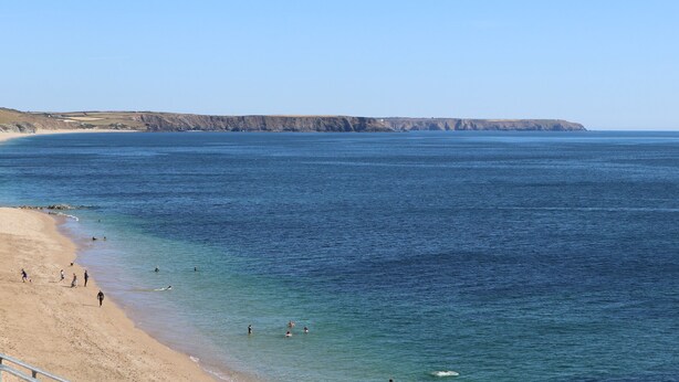 Una playa costera con aguas azules cristalinas, orilla arenosa y acantilados al fondo.