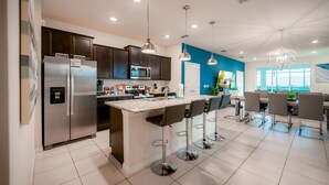 A modern kitchen with dark cabinets, stainless steel appliances, and a central island with bar stools. - Luxury 7 Bed w/Pool, Home Theater, & Themed Gameroom! (Davenport)