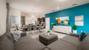 A modern living room with grey sofas, a dining area, and a kitchen in the background. - Luxury 7 Bed w/Pool, Home Theater, & Themed Gameroom! (Davenport)