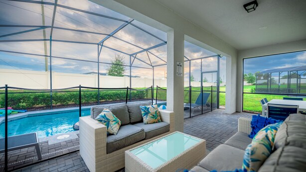 A covered patio area with a pool, outdoor furniture, and a view of the surrounding landscape. - Luxury 7 Bed w/Pool, Home Theater, & Themed Gameroom! (Davenport)