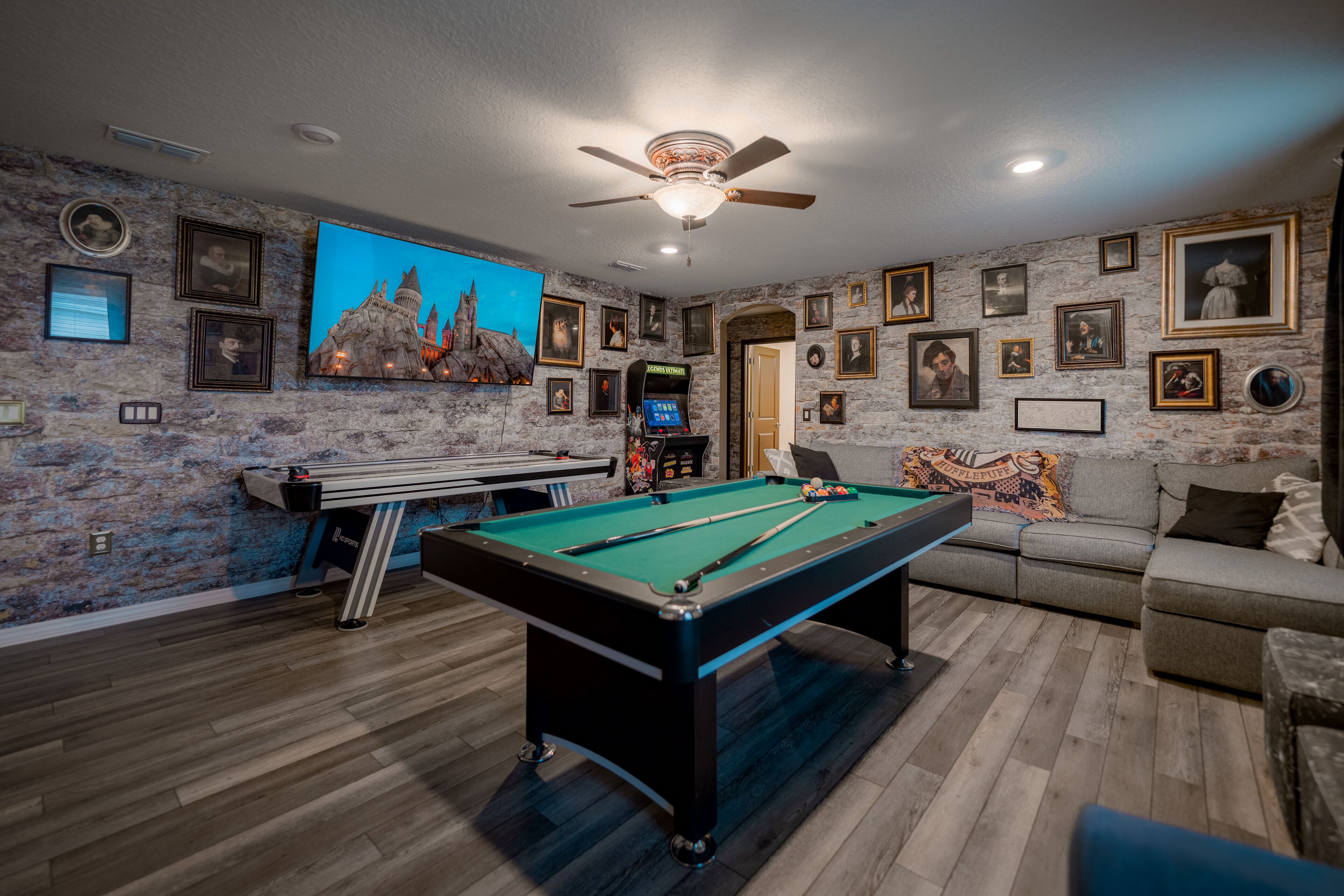 A pool table in a room with stone walls, a sofa, and framed pictures.