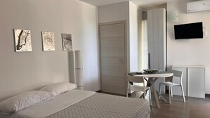 A modern bedroom with a bed, a desk with a chair, and a TV on the wall.