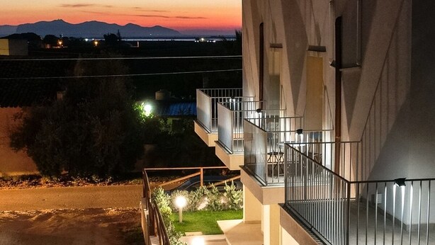 A modern building with a balcony, a pathway with lights, and a view of distant mountains at dusk.